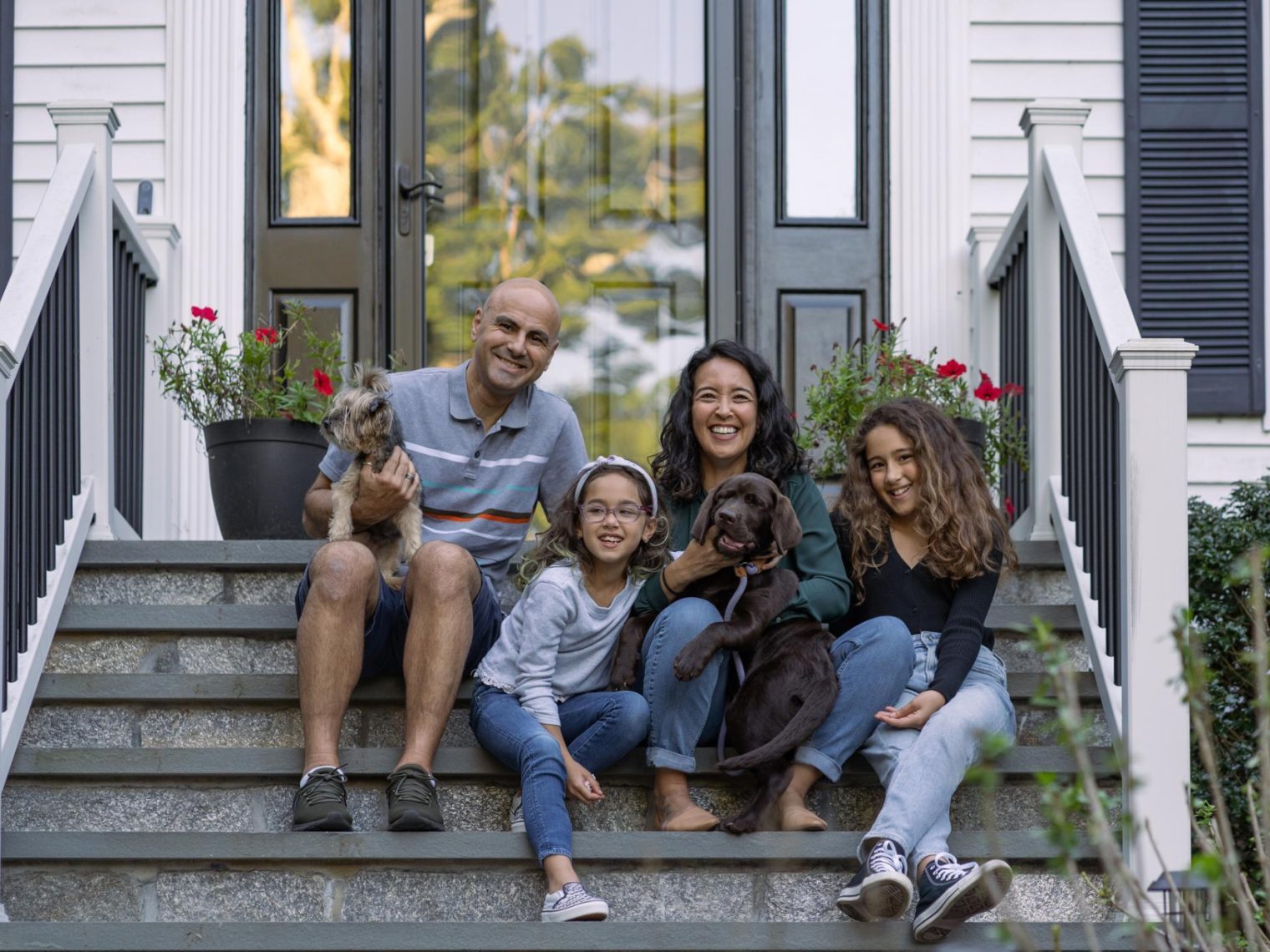 A family sitting on the steps of their house with their two dogs.
