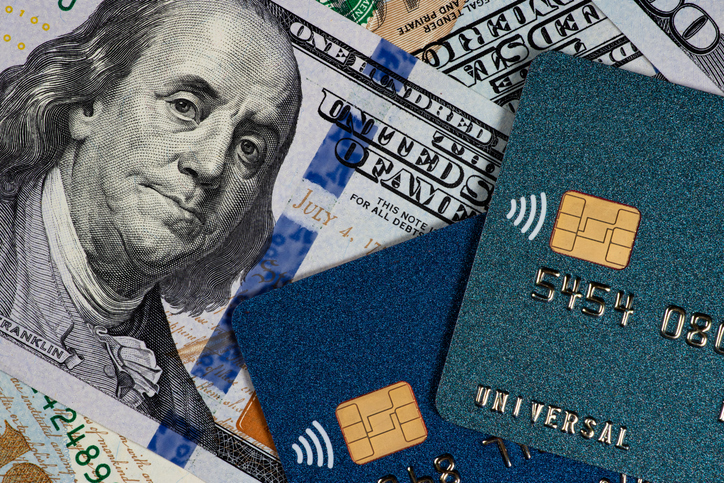 A close-up view of various denominations of U.S. dollar bills with the portrait of Benjamin Franklin visible, overlaid with two credit cards.