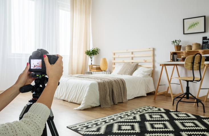 A person is taking a photo with a DSLR camera on a tripod, capturing a well-decorated bedroom with a cozy, modern design, possibly for a real estate listing.