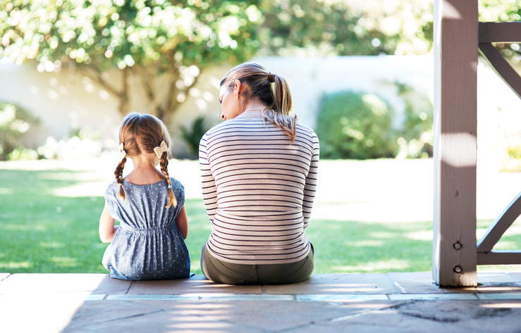 A woman and a young girl, likely mother and daughter, sitting side by side on the porch, looking out into the garden, sharing a quiet moment together.